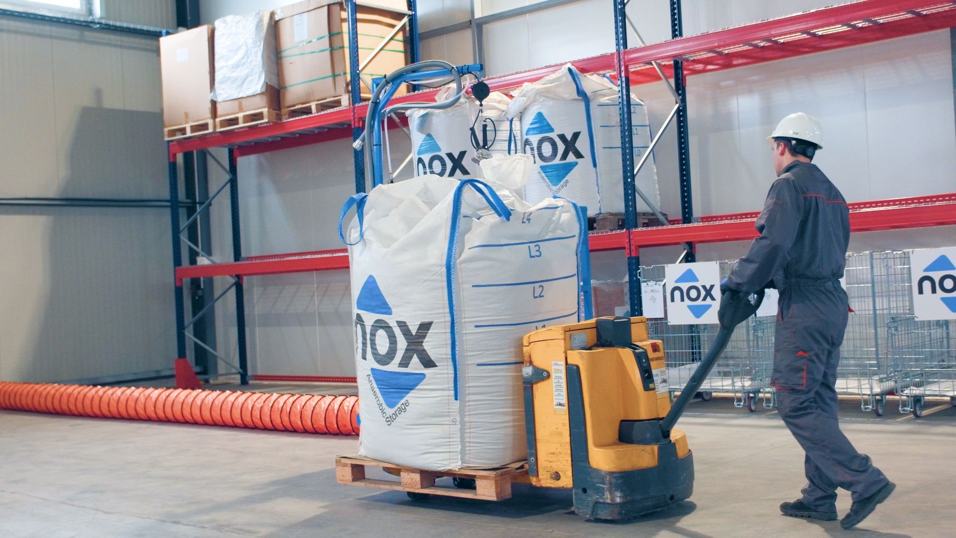 Operatore con transpallet elettrico movimenta Nox Big Bag ermetico in magazzino con scaffalature Operatore con transpallet elettrico movimenta Nox Big Bag ermetico in magazzino con scaffalature