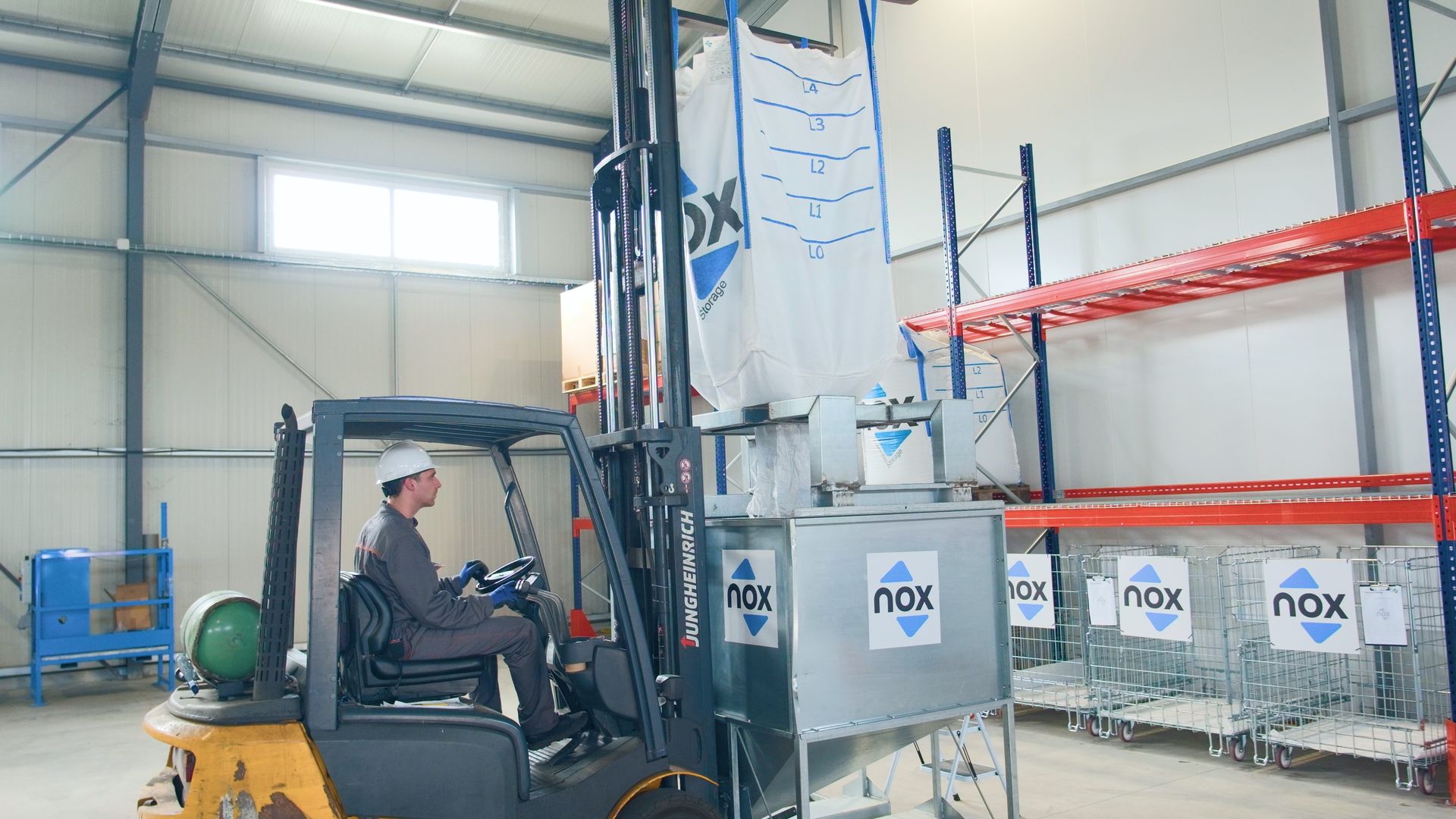Operatore con carrello elevatore posiziona Nox Big Bag ermetico su tramoggia di scarico in magazzino Operatore con carrello elevatore posiziona Nox Big Bag ermetico su tramoggia di scarico in magazzino